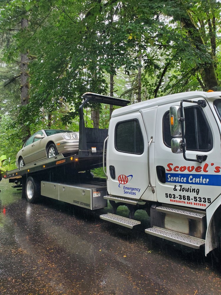 Scovel's white flatbed tow truck carrying a vehicle, with red and blue lettering and the phone number 503-368-5335 on the door.